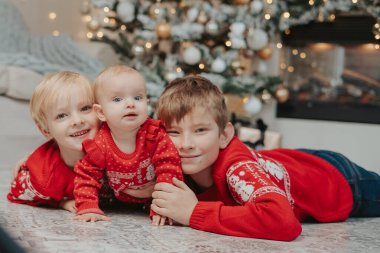 Mutlu aile çocukları, erkek ve kız kardeşler Noel ağacının yanında yere gülüyorlar.