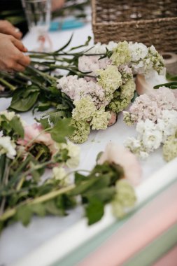 Çiçeklerle dolu bir masa ve buket yapmak için malzeme.