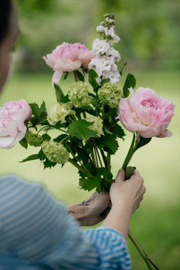 Kadın elleri çiçek atölyesinde şakayıkla buket yapar.