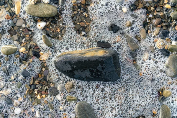 海岸沿いの様々な小石や泡 ビューを閉じる — ストック写真