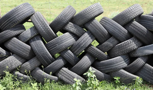 Old car tires in row as a fence  in a rural courtyard. Old tires functions as a protective fence. Household waste. Environmental disaster.  Old tires as garbage on the ground