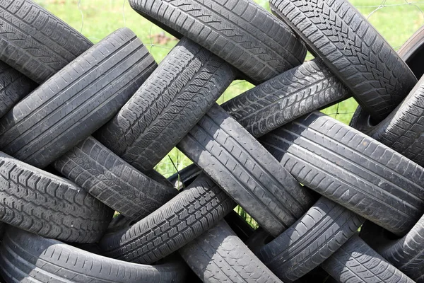 Old car tires in row as a fence  in a rural courtyard. Old tires functions as a protective fence. Household waste. Environmental disaster.  Old tires as garbage on the ground
