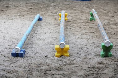 Atlama direklerini, engelleri, engelleri göster. Atlama eğitiminde yarışçıları bekle. Yaz mevsiminde dışarıda at yarışı kursu. Binicilik merkezindeki kumda kutuplar var.