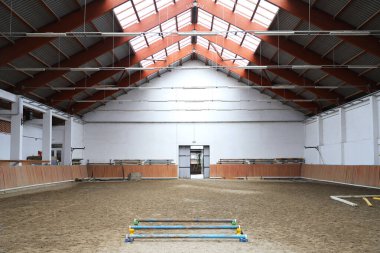 Modern kapalı alanda at eğitimleri için kum kaplama alanı. Boş, ferah binicilik salonu manzarası. Pencerelerden güneş ışığı geliyor. Modern binicilik mekanları