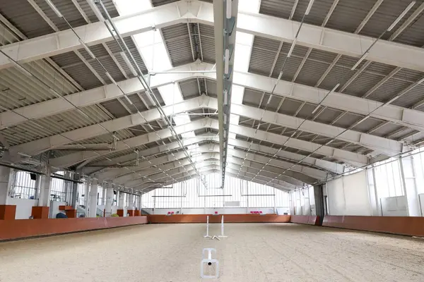 stock image Modern indoor riding arena covering sand for horse trainings. Empty spacious riding hall interior view. Sunlight through windows. Modern equestrian place indoors