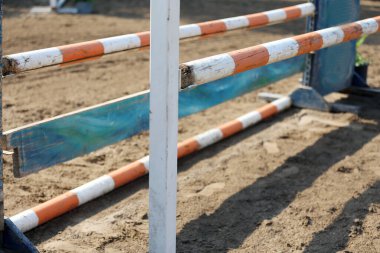 Atlama direklerini, engelleri, engelleri göster. Atlama eğitiminde yarışçıları bekle. Yaz mevsiminde dışarıda at yarışı kursu. Binicilik etkinliği için kumda kutuplar