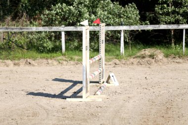 Atlama direklerini, engelleri, engelleri göster. Atlama eğitiminde yarışçıları bekle. Yaz mevsiminde dışarıda at yarışı kursu. Binicilik etkinliği için kumda kutuplar