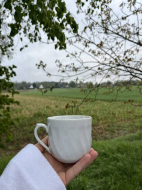 Elinde fincanla yeşil bir bahçenin arka planında