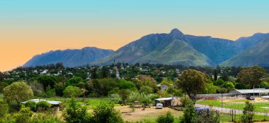 Panoramic view of the historic town of Swellendam, nestled amidst lush greenery and the majestic Langeberg Mountains in the Western Cape, South Africa, on a clear spring day. clipart