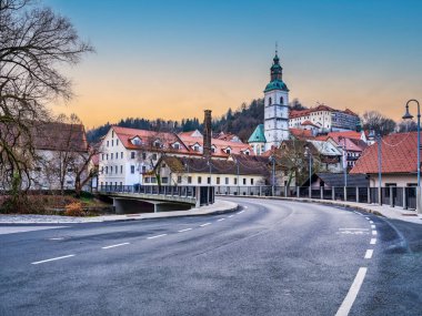 Slovenya 'nın Skofja Loka köyünde gün batımında dolambaçlı bir caddede eski binalar ve Kapucinski samostan kilise kulesi