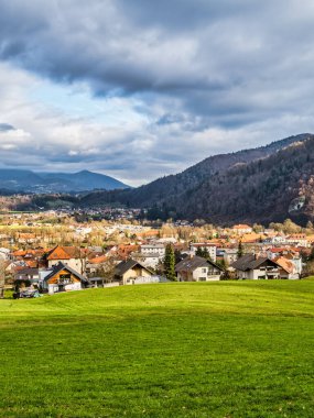 Kamnik köyü vadisinin dikey görüntüsü, yemyeşil çimen tarlası ve arka planda dramatik bulutlarla dolu dağ, Kamnik, Slovenya