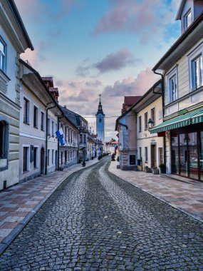 Cobblestone Sutna caddesindeki renkli bulutlu eski ev ve dükkanların dikey çekimi, Kamnik, Slovenya