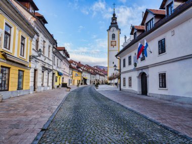 Kaldırım taşı Sutna sokağı, eski binalar ve mavi gökyüzü olan Cerkveni kilise kulesi, Kamnik, Slovenya