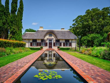 Hollanda Burnu binası ve havuz kenarındaki su havuzu Vergelegen Şarap Malikanesi, Somerset West, Güney Afrika 'da yemyeşil bahçe ve ağaçlarla çevrili.