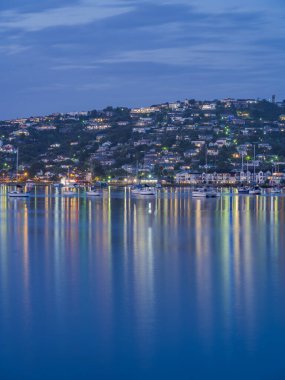 Knysna Lagün Limanı 'nın portresi ve gün batımından sonra şehrin renkli ışıkları su yüzeyine yansıyor.