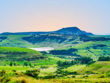 Drakensberg vadisi, baraj ve gün batımında dağın kenarındaki bir köy manzarayı ve sakin manzarayı gözler önüne seriyor, KwaZulu-Natal, Güney Afrika