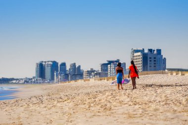 Arka planda Blouberg silueti olan Sunset Beach 'te yürüyen iki Afrikalı genç kız, Cape Town, Güney Afrika