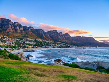 Cape Town, Güney Afrika 'da günbatımında altın bulutlar ve canlı mavi gökyüzü ile Kamp Koyu' na bakan görkemli 12 Havari Dağı.