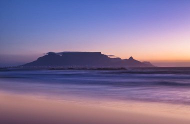 Güney Afrika Cape Town yakınlarındaki mavi saatte Masa Dağı 'nın dingin güzelliğini gösteren uzun pozlu bir fotoğraf..