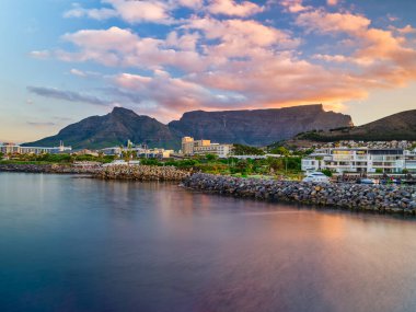 Cape Town, Güney Afrika 'da gün batımının altın rengi ile aydınlatılan dramatik bulutlarla Fare Noktası' ndan Masa Dağı 'nın nefes kesici bir görüntüsü..