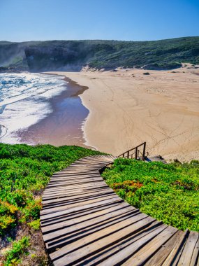 Robberg Yarımadası 'nın kumlu sahilinden başlayıp, Plettenberg Körfezi, Güney Afrika' daki doğal koruma alanına doğru uzanan tahta bir geçide dikey bir perspektif.