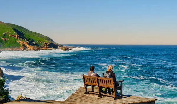 Bir çift bankta oturuyor, panoramik okyanus manzarasında ve Robberg Doğa Rezervi 'nde huzurlu bir atmosferde, Plettenberg Körfezi, Güney Afrika