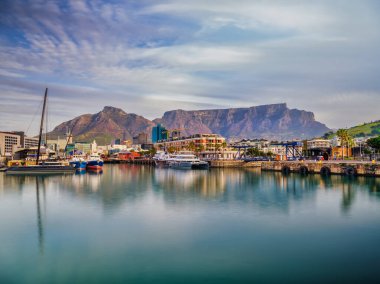 Gün batımında canlı V & A Rıhtımı 'nı çeken güzel bir uzun pozlama çekimi, Güney Afrika' daki Cape Town, Masa Dağı 'nın ikonik siluetine karşı, ipeksi, pürüzsüz su ve ışık yolları oluşturur.