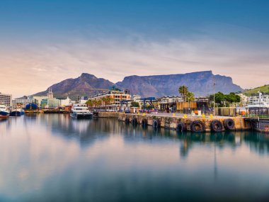 V & A Rıhtım Limanı 'nın büyüleyici uzun pozlama görüntüsü, bulanık tekne hareketleri ve parıldayan yansımalar, Cape Town silueti ve arka planda ikonik Masa Dağı, Güney Afrika