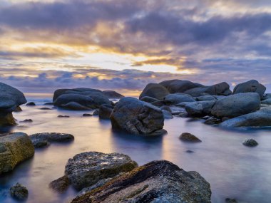 Clifton sahilindeki ikonik kayalar arasında ipeksi, pürüzsüz suya yansıyan renkli günbatımını uzun süre görüntüler. Cape Town, Güney Afrika
