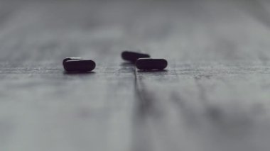 Kara haplar ahşap masaya ağır çekimde düşüyor. İlaç, sürükleme, bağımlılık. Kapat.