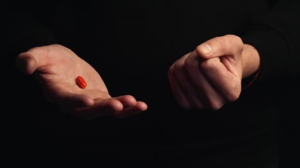 スタジオショット男性の手は黒の背景に隔離された赤い錠剤を示しています 正しい選択をするという概念 シネマティック4K映像 — ストック動画