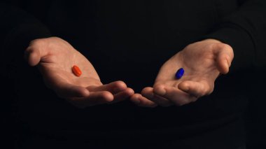 Stüdyoda erkek eli, siyah arka planda kırmızı ve mavi haplar gösteriyor. Doğru seçim yapma kavramı.