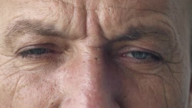 Gerçekten olgun, kırışıklıkları olan orta yaşlı bir adamın yakın plan portresi. Güzel mavi gözlerini açıyor ve doğruca kameraya bakıyor.