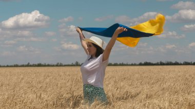 Ukraynalı vatansever kadın buğday tarlasında duruyor ve elinde Ukrayna 'nın mavi-sarı bayrağını tutuyor.