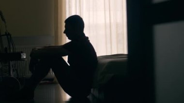 Yerde oturan depresif bir adamın silueti. Mutsuz bir insan yatak odasında bir şeyler düşünüyor.