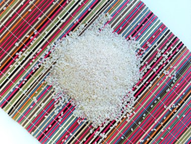 Renkli bir hasırın üzerine saçılmış pirinç, bir avuç pirinç.