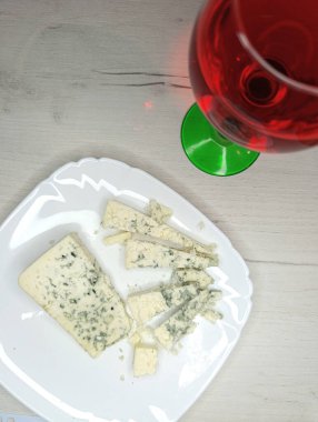 Beyaz kare tabakta Dorblu mavi peynir. Gri ahşap arka planda. Bir kadeh kırmızı şarapla.