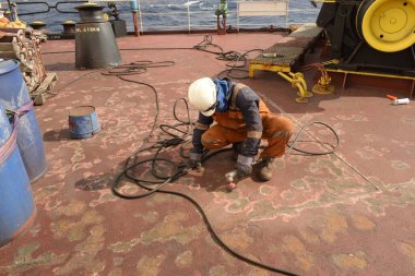 Denizde, gemide - 21 Aralık 2022: Ticari kargo gemisinin mürettebatı güverte bakımını yaparken geminin kaka güvertesinde öğütücü makine kullanarak cilalanıyor.