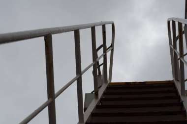 Bir geminin konaklama yerinin dışındaki merdiven gökyüzüne ulaşarak biriken savaşı sembolize eder.