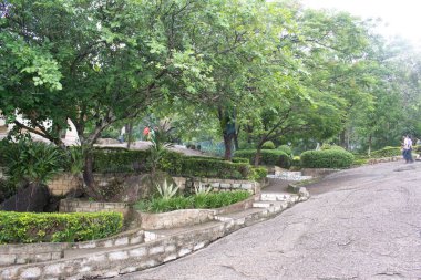 rock garden, ranchi, jharkhand, india - july 14, 2024 : walkway surrounded by decorative structures holding abundant greenery all over with scattered visitors inside the park clipart