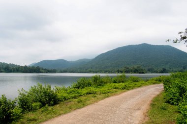 Arka planda bol yeşillik ve mistik tepelerle dolu huzurlu topchachi gölünün yanında yıpranmış bir yol.