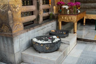 flowers offered on some of sacred stone alter where lord buddha kept his feet while circling the bodhi tree while meditating at mahabodhi temple, bodh gaya, bihar, india clipart