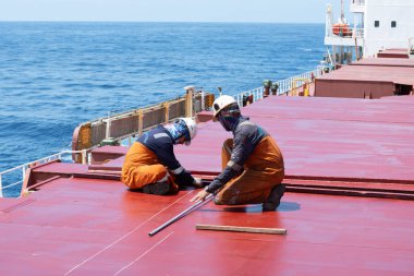 at sea, on board ship - january 02, 2025 : crewembers of ship preparing marking on newly painted cargo hold cover clipart