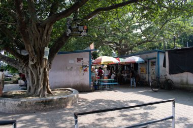 Chandannagar ipliği, hoogly, West Bengal, Hindistan - 23 Temmuz 2025: Büyük ağaç yaprakları altında gölgelenmiş insanlarla küçük lokantalar