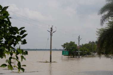 Tamluk nehir kenarı, doğu medinipur, batı bengal, Hindistan-Ağustos 11, 2025: elektrik direklerini, sualtı ağaçlarını ve kısmen sualtı yapılarını, ticari uyarı ve yerel Bengalce dilinde reklam panolarını gösteren sular altında kalmış manzara