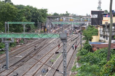 Sonarpur, Batı Bengal, Hindistan - 27 Temmuz 2025: Muson mevsiminde Hindistan 'da yoğun bir demiryolu kavşağının samimi görüntüsü, yerliler üstteki yaya köprüleri ve istasyon levhalarıyla birden fazla ray boyunca yürüyorlar.