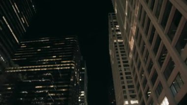 Geceleri şehir merkezindeki yüksek ofis binaları arasında araba kullanmak. Yavaş çekim, düşük açı görüş, doli çekim. 