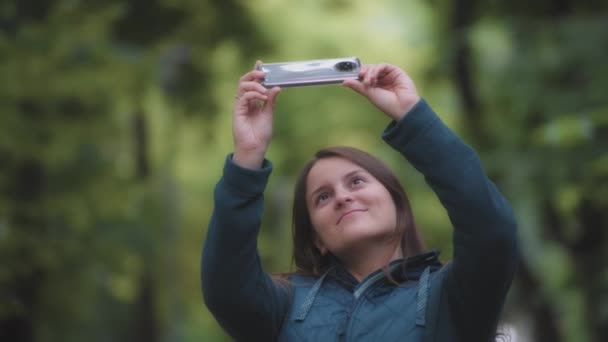 Eine Lächelnde Frau Fotografiert Die Bäume Mit Einem Handy Der — Stockvideo
