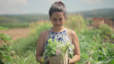 Elinde sebze ve yenilebilir çiçeklerle dolu bir sepet tutan gülümseyen kadın. Yavaş çekim, yüzeysel alan derinliği.