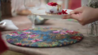 Renkli bir paspasın üzerinde kırmızı çiçeklerle servis edilen gurme tatlısı. Yavaş çekim, yüzeysel alan derinliği.